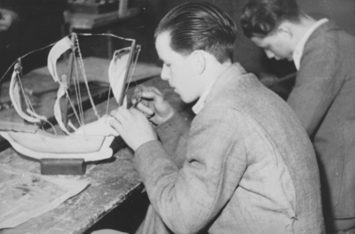 876577 Portret van een jongen, lid van een 'huisvlijtclub' van het St. Franciscus Liefdewerk, die een modelbootje aan ...